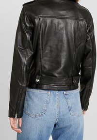 Czarna skórzana kurtka motocyklowa o dopasowanym kroju, z suwakiem na rękawach i metalowymi detalami. Zestawiona z niebieskimi jeansami z wysokim stanem.