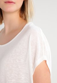 Camiseta blanca de manga corta con un corte holgado y una textura suave y ligera. Cuenta con un escote redondo y hombros ligeramente caídos.