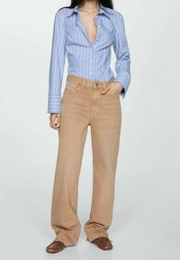 Camicia a righe blu chiaro con bottoni e maniche lunghe, abbinata a jeans in denim beige larghi e scarpe slip-on marroni.
