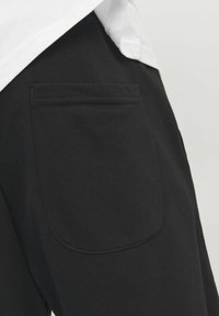 Svarta sweatpants har en bakficka med en rund, mörknad design. Tyget är slätt, med en mjuk textur som passar för avslappnad användning.
