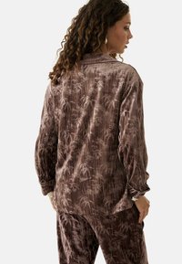 Conjunto de loungewear marrón de terciopelo que presenta un patrón de hojas de palma, con mangas largas y un ajuste relajado. Superficie texturizada con un ligero brillo.