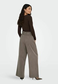 Bruine lange mouwen top gecombineerd met hooggesneden, wijde grijs gestreepte broek. De broek heeft een tailleband met riem en een gestructureerde stof.