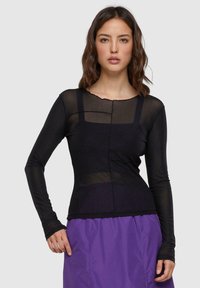 Langärmliges schwarzes Oberteil mit durchscheinendem Design, das über einen runden Ausschnitt, strukturierten Vordernähten und eine enganliegende Silhouette verfügt.