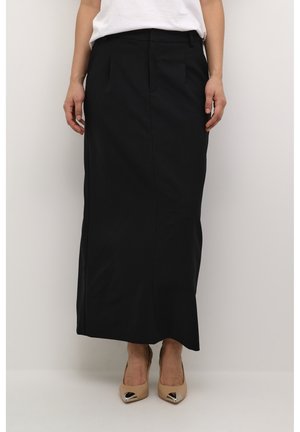 Jupe noire mi-longue en tissu lisse avec une coupe ajustée. Elle possède des poches avant et un design de coutures épurées, associée à des talons beiges.