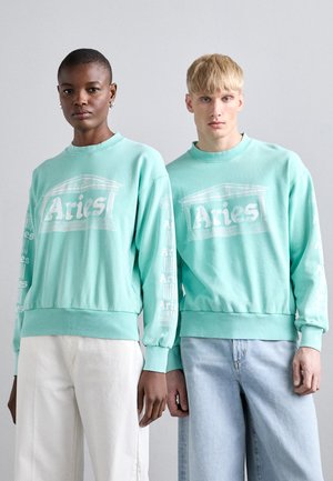 Dwa modele noszą miętowozielone bluzy z białym napisem "Aries" na przodzie i rękawach. Bluzy mają prążkowane mankiety i dół.