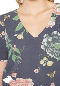 Top com estampa floral apresentando um fundo azul-marinho, decote em V, mangas curtas e flores e borboletas multicoloridas por todo o tecido.
