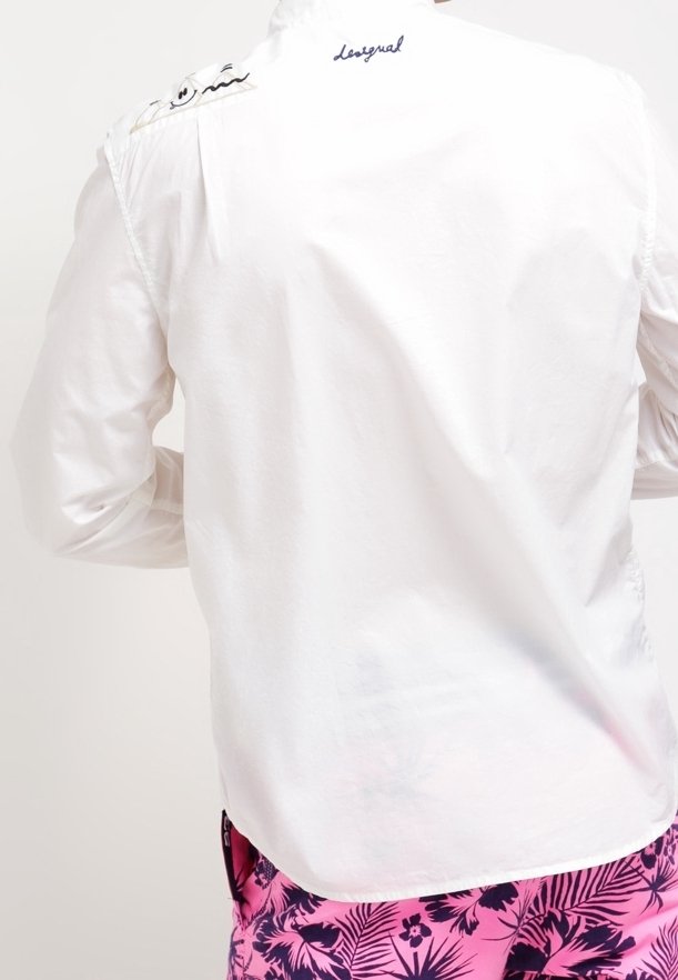 Vit skjorta med knappar framtill, med en slät textur, broderade detaljer på axeln och en synlig varumärkeslogotyp på baksidan.