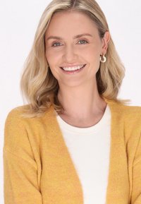 Un cardigan giallo, con texture, indossato sopra una maglietta bianca a costine. Il cardigan presenta un'apertura frontale e maniche lunghe, dando un aspetto accogliente.