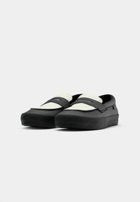 Schwarze Slipper mit einem strukturierten weißen Obermaterial, runder Zehenpartie und einer dickeren Gummisohle. Minimalistisches Design ohne sichtbares Branding.
