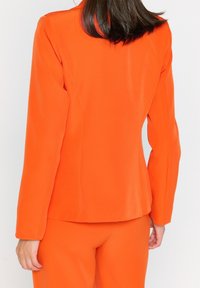 Orange tailored blazer with long sleeves, smooth texture, and a structured silhouette, paired with matching trousers in the same color.