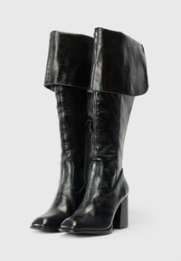 Μαύρες δερμάτινες μπότες έως το γόνατο με διπλωμένα μανίκια, πλαϊνές φερμουάρ και κομψές τετράγωνες τακούνια, που βρίσκονται σε λευκό φόντο.