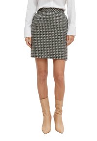 Jupe pied-de-poule noire et blanche à coupe près du corps, longueur genou, avec une taille haute et un tissu texturé. Associée à des bottes à talons nude.