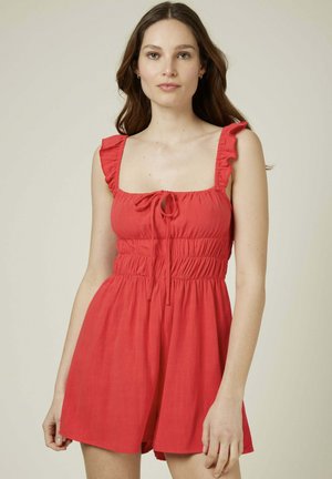 Robe d'été rouge avec un décolleté carré, des bretelles à volants et un lien ajustable à l'avant. Présente une taille smockée et un short ample.