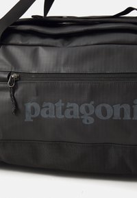 Black Patagonia shoulder bag with a front zipper pocket and visible fabric texture, shown against a white background.