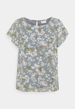 Blommig topp i ljusblått, med korta ärmar, rund hals och en nyckelhålsknäppning i ryggen. Mönstret inkluderar vita och gröna blommor.