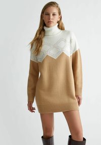 Maglione con collo alto lavorato a maglia, caratterizzato da una parte superiore color crema e una parte inferiore color beige. Il design presenta un motivo geometrico con accenti texturizzati.