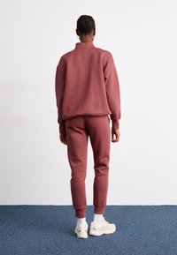 Sweatshirt och joggers i en dammig rosafarv, tillverkade av mjukt material. Kläderna har en avslappnad passform och ribbade manschetter, tillsammans med ljusa sneakers.