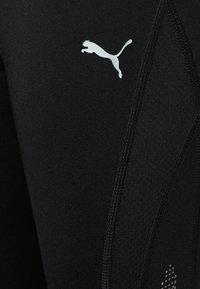 Czarne legginsy sportowe z elastycznego materiału, z białym logo Puma i teksturowanym wykończeniem wzdłuż szwu bocznego.