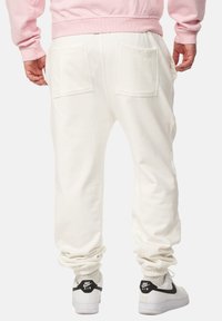 Weiße Jogginghosen mit elastischem Bund, zwei Gesäßtaschen und Bündchen, kombiniert mit weißen Nike-Sneakern mit schwarzen Akzenten.