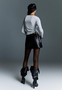 Šedý dlhý rukáv top, čierna kožená mini sukňa, čierne čižmy po kolená s preloženým detailom. Hladký textilný materiál, priliehavý strih.