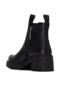 Botas cortas de cuero negro con punta redonda, cierre lateral con cremallera y tacón grueso. Presentan tiradores de tela en la parte posterior.