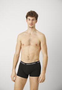 Schwarze Boxer Shorts für Männer mit einem weißen Logo-Bund, aus flexiblem Material gefertigt, in passgenauer Form und mittlerer Oberschenkellänge.