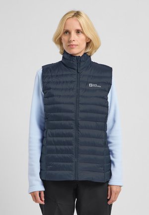 Marineblauer gepolsterter Weste mit hohem Kragen und Reißverschluss, mit horizontalen Nähten, getragen über einem hellblauen Langarmshirt.