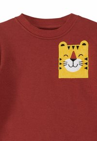 Bordeauxfarbenes Sweatshirt mit einem gelben, gestickten Tigerkopf auf der Brust. Rundhalsausschnitt und weicher, strukturiert Stoff.