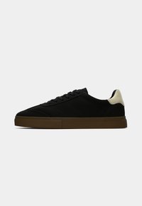 Adidași negri din suede cu un profil jos, având o talpă din cauciuc bej și un accent contrastant de crem la călcâi. Vârf rotund și design cu șireturi.