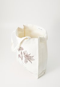 Canvas tygpåse i krämfärg, med en brun blommig illustration. Två tyghandtag med öppen topp och minimalistisk design.