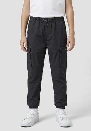 Zwarte cargobroek met elastische taille en enkels, zijvakken met klep, gedragen met witte sneakers en een wit overhemd.