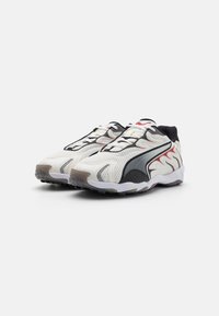 White and black sporty sneakers with mesh upper, textured accents, vibrant red detailing, and rubber sole featuring a wavy design.