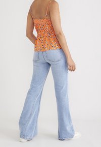 Orange blommig linne med justerbara axelband, parat med avslappnade ljusblå denimjeans och vita sneakers.