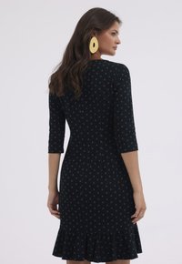 Czarna sukienka w turkusowe kropki, z 3/4 rękawami, dopasowanym stanem i falbanistym dołem. Miękka faktura i gładki materiał.