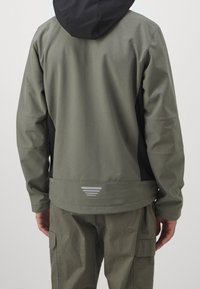 Khaki ja must kapuutsiga jope sileda tekstuuriga. Omab peegeldavaid detaile ja kõverat allserva. Tagapool vaade kihilise disainiga.