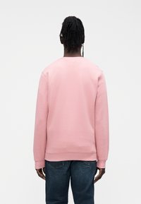 Sweatshirt rosa com gola redonda e punhos canelados, feita de tecido macio de mistura de algodão, usada com jeans de ganga azul.