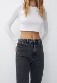 Haut blanc court à manches longues associé à un jean denim gris foncé taille haute, présentant un design classique à cinq poches et un léger effet délavé.