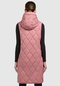 Padded pink vest mit einem gesteppten Rautenmuster, das bis zur Mitte des Oberschenkels reicht, mit einer großen Kapuze und einem schwarzen Langarmshirt darunter.