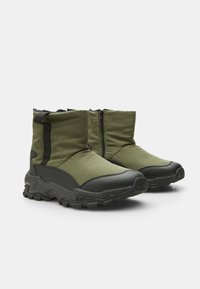 Botas de tobillo acolchadas verdes con suelas de goma negra, un cierre lateral de cremallera y acentos texturizados. Livianas, con un diseño contemporáneo y elegante.