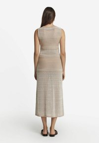 Stickad beige klänning med en åtsittande bodice och en utställd midilång kjol med ett strukturerat mönster. Bärs med mörka sandaler.