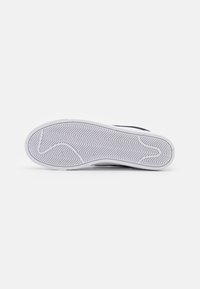 Svart sneaker med en hvit gummisåle som viser et fiskebensmønster. Designet har minimal detaljering på overdelen.