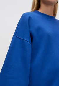 Königsblaues, übergroßes Sweatshirt mit rundem Halsausschnitt und überschnittenen Schultern. Glatte Textur mit minimalen Nähten.