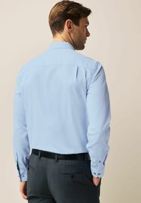 Chemise à manches longues bleu clair avec un motif texturé, col standard et poignets boutonnés, assortie à un pantalon gris et une ceinture noire.