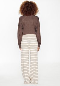 Pull court marron à manches longues associé à un pantalon beige à jambes larges avec des rayures blanches horizontales ; texture douce et tricotée.