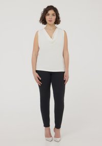 Top bianco senza maniche con scollo drappeggiato, abbinato a jeans scuri aderenti e décolleté argento a punta. Design semplice e texture liscia.