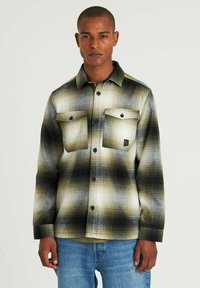 Camicia di flanella a quadri nei toni di crema, oliva e nero; presenta due tasche sul petto, chiusura con bottoni e una vestibilità comoda.