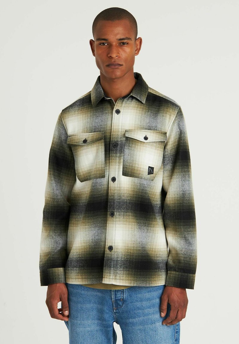 Camicia di flanella a quadri nei toni di crema, oliva e nero; presenta due tasche sul petto, chiusura con bottoni e una vestibilità comoda.