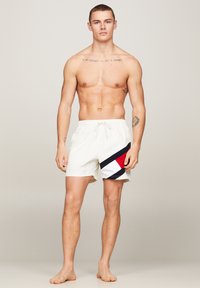 Pantaloni da bagno bianchi con cintura elastica, caratterizzati da un design diagonale in nero, rosso e blu. Tessuto leggero con una finitura liscia.