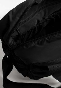 Borsa in tessuto nero con numerosi scomparti con zip, un interno morbido e testurizzato, e una tracolla larga e regolabile.