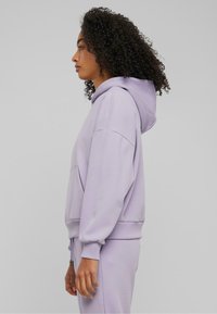 Hoodie lilas avec une capuche spacieuse, poche kangourou et manches à revers. Fabriqué à partir d'un tissu doux, offrant une coupe décontractée et une texture lisse.